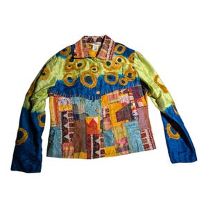 May include: A long-sleeved jacket featuring a patchwork design with various fabric textures and colors including lime green, blue, yellow, and orange. The upper section displays embroidered gold circular motifs, while the lower body consists of rectangular fabric panels with visible stitching. It has a collared neckline and a front button closure.