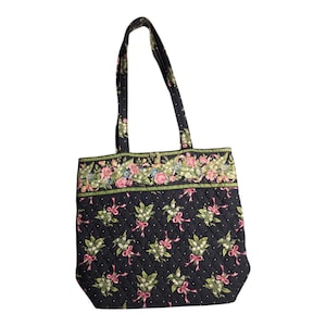 Puede incluir: Bolso tote acolchado negro con un estampado floral y de lazo. El bolso presenta un borde superior con flores rosas y azules y detalles verdes. Tiene dos asas y está diseñado para transportar objetos.