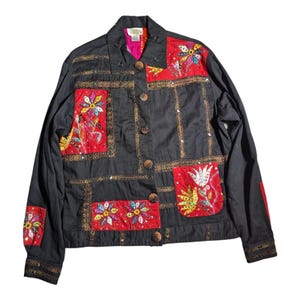 May include: Black jacket with floral embroidery and sequin accents. The jacket features red patches with colorful flower designs and gold trim. It has button closures and a collared neckline, creating a unique, artistic look.
