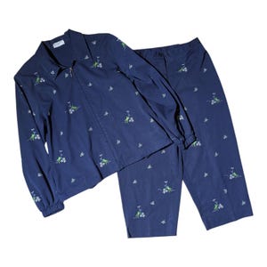 May include: A navy blue two-piece set consisting of a long-sleeved zip-up jacket and matching trousers. The fabric features an embroidered pattern of small white flowers and light green frogs throughout the entire garment, including the sleeves.