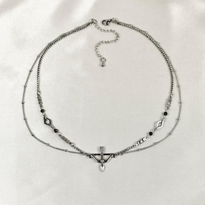 May include: A silver layered necklace with a bow and arrow pendant. The necklace has small black beads and diamond-shaped charms.