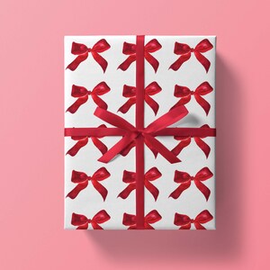 May include: White gift wrap with a repeating pattern of red watercolor bows. A red ribbon is tied around the box.
