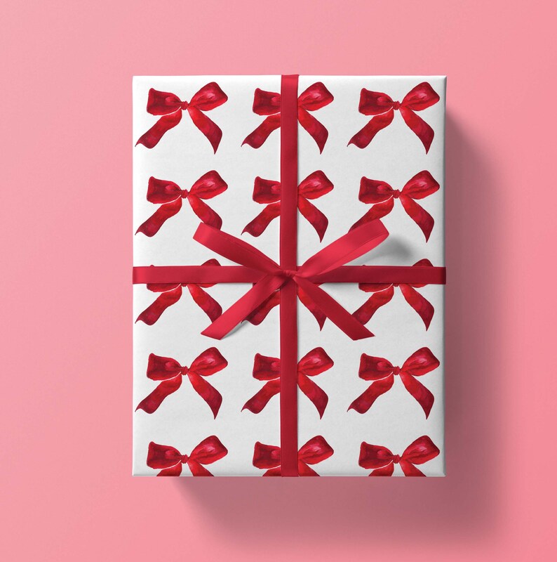 May include: White gift wrap with a repeating pattern of red watercolor bows. A red ribbon is tied around the box.