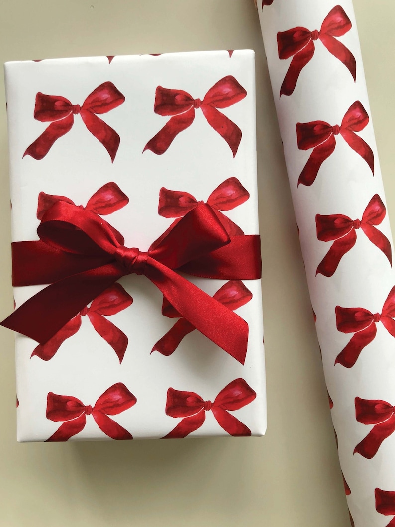 May include: White wrapping paper with a repeating pattern of red watercolor bows. A red satin ribbon is tied around the paper.