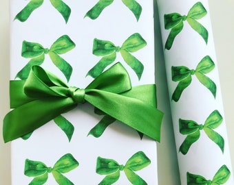 May include: Green watercolor bow pattern wrapping paper with a green satin ribbon tied around a gift box. The wrapping paper has a repeating pattern of green bows on a white background.