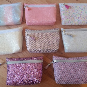 May include: Eight small zippered pouches with glitter fabric in various colours and patterns, including pink, white, rainbow, and gold. Each pouch has a small tassel zipper pull.
