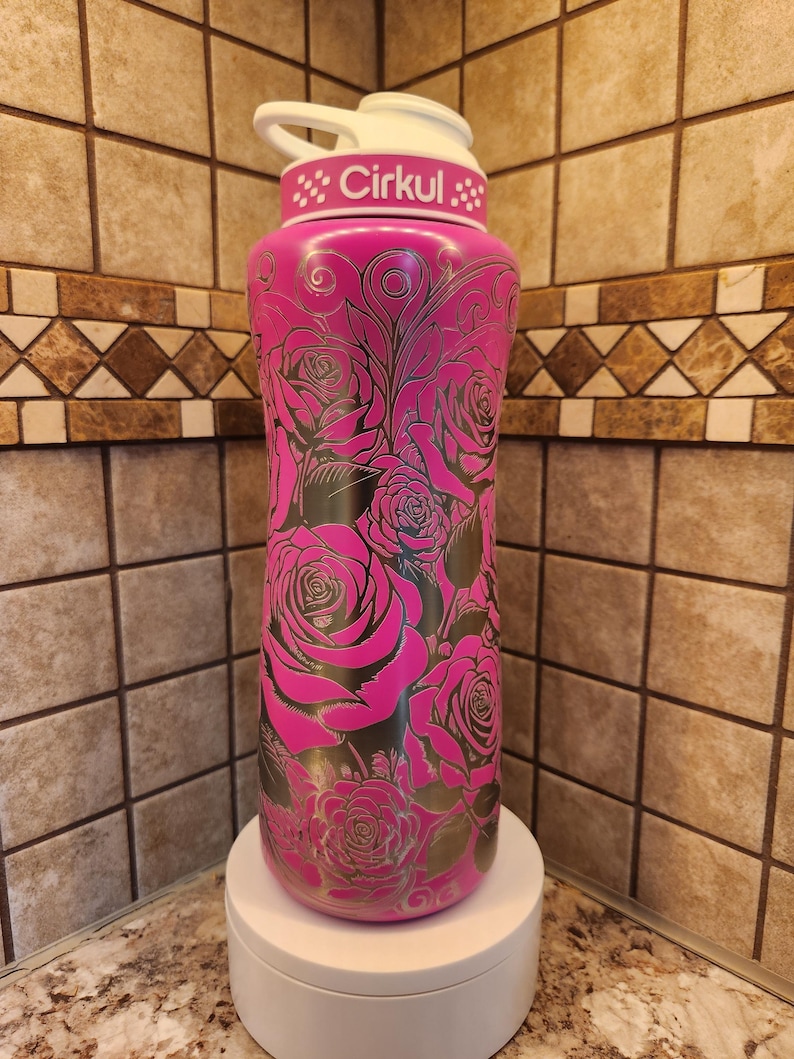 Pu&ograve; includere: Una borraccia rosa isolata con coperchio e manico bianchi. La bottiglia &egrave; decorata con un motivo a rose e la scritta "Cirkul". La bottiglia &egrave; su un supporto bianco.