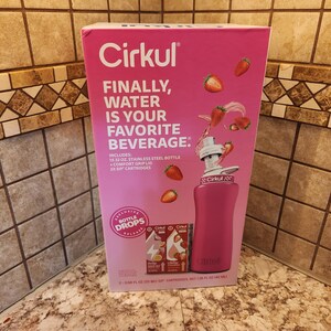Pu&ograve; includere: Un kit di bottiglia d'acqua Cirkul rosa con la scritta "FINALLY, WATER IS YOUR FAVORITE BEVERAGE." Il kit include una bottiglia in acciaio inossidabile da 946 ml, coperchio con impugnatura confortevole e due cartucce per sorseggiare. Le fragole sono mostrate sulla scatola.