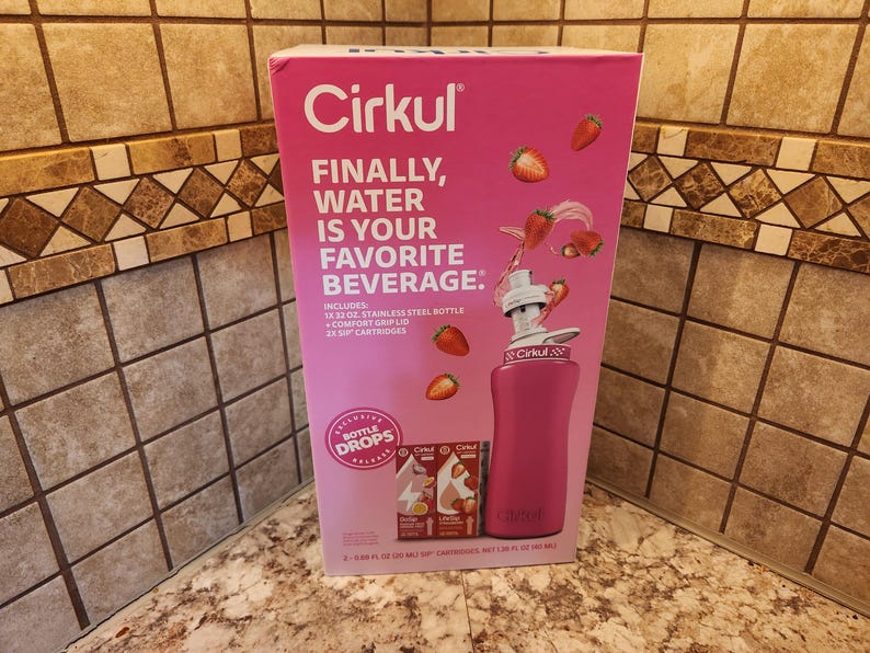 Pu&ograve; includere: Un kit di bottiglia d'acqua Cirkul rosa con la scritta "FINALLY, WATER IS YOUR FAVORITE BEVERAGE." Il kit include una bottiglia in acciaio inossidabile da 946 ml, coperchio con impugnatura confortevole e due cartucce per sorseggiare. Le fragole sono mostrate sulla scatola.