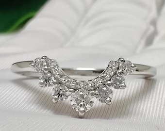 May include: A delicate silver ring with a curved design featuring a row of small diamonds and larger diamonds at the top, creating a crown-like effect.