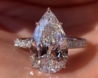 May include: A pear-shaped diamond engagement ring with a pave setting on the band. The ring is set in white gold.