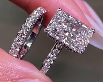 May include: A silver engagement ring set with a large, rectangular, clear diamond. The ring is set with smaller diamonds around the band.