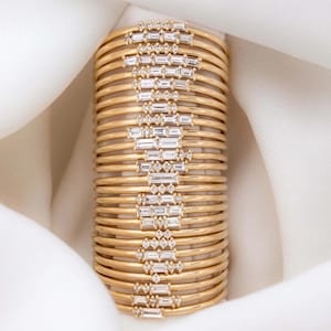 May include: A stack of gold bangles with a row of small diamonds on each bangle.