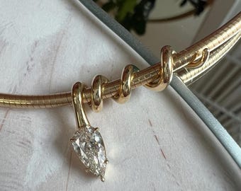 May include: A gold-toned omega chain necklace featuring a flexible, coiled design that wraps around the band. A single pear-shaped, faceted clear stone pendant hangs from the center, secured by a polished gold-toned metal bail.