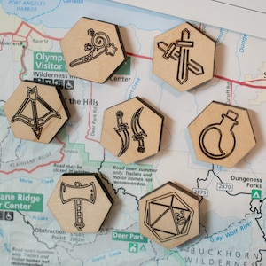 May include: Six wooden hexagonal tokens with different symbols, including a sword, a potion bottle, a bow and arrow, a dagger, an axe, and a 20-sided die, on a map of the Olympic National Forest.