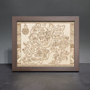May include: A framed, detailed map with a dark brown wooden frame. The map is light brown and features intricate illustrations of a fantasy world, including landmasses, cities, and text. A compass rose is visible in the upper left corner. The frame is rectangular.