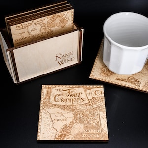 May include: Set of six wooden coasters featuring maps from the fantasy novel "The Name of the Wind" by Patrick Rothfuss. The coasters are in a wooden box with the title "The Name of the Wind" engraved on the front. One coaster features a map of "The Four Corners of Civilization".