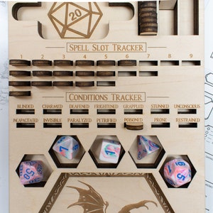 May include: A wooden game board with a dragon design, used for tracking spell slots and conditions in a tabletop role-playing game. The board has a grid of slots for spell slots, a section for tracking conditions, and a space for dice. There are five dice on the board, all with a pink and blue swirl pattern.