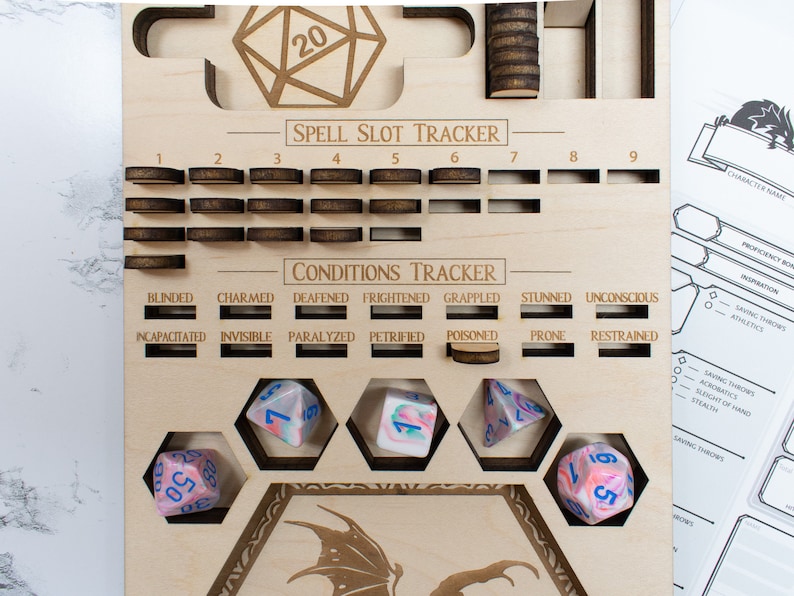 May include: A wooden game board with a dragon design, used for tracking spell slots and conditions in a tabletop role-playing game. The board has a grid of slots for spell slots, a section for tracking conditions, and a space for dice. There are five dice on the board, all with a pink and blue swirl pattern.