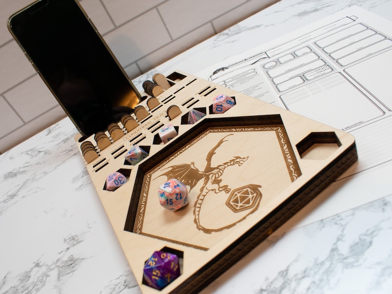 May include: A wooden dice tray with a dragon design and compartments for dice. The tray has a phone stand and a separate area for dice rolling. There are several colorful dice on the tray.