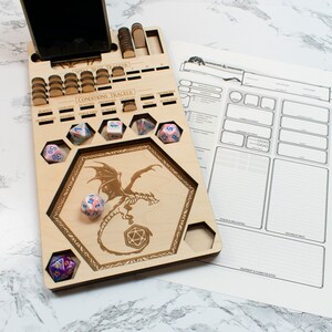 May include: A wooden gaming tray with a dragon design and compartments for dice. The tray has a phone holder and a section for tracking conditions. There are several dice on the tray, including a d20, a d6, and a d4.