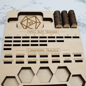 May include: Wooden game board with a 20-sided die, spell slot tracker, and condition tracker. The board has slots for tokens and is engraved with the words "SPELL SLOT TRACKER" and "CONDITIONS TRACKER".