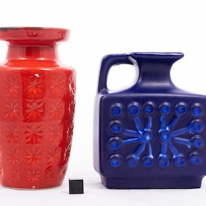 Könnte beinhalten: Zwei Keramikvasen, eine rote und eine blaue, mit einem geometrischen Muster. Die rote Vase hat ein Blumenmuster und die blaue Vase hat ein Sternmuster.