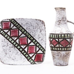 Peut inclure: Un pichet et une assiette carrée en céramique blanche avec un motif géométrique dans des tons de rouge, vert et marron. Le motif présente une série de carrés et de triangles.