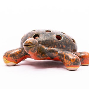 May include: A ceramic turtle figurine with a brown and orange glaze. The turtle has holes in its shell, suggesting it may be a flower pot or a decorative holder.