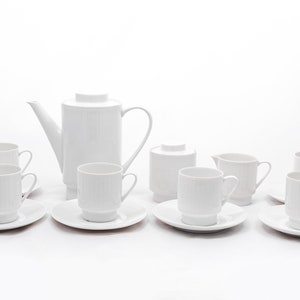 Puede incluir: Un juego de té de porcelana blanca con una tetera, una jarra de crema, un azucarero y seis tazas y platillos.