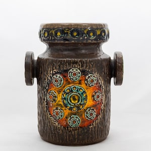 May include: A brown ceramic vase with a textured surface and a colorful circular design. The vase has two side handles and a decorative pattern of circles in shades of orange, yellow, and blue. The vase is approximately 8 inches tall.