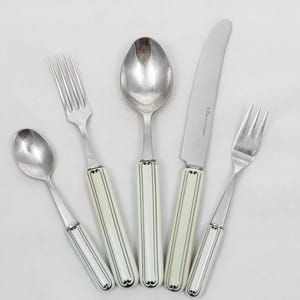 Puede incluir: Un juego de cinco cubiertos, que incluye dos tenedores, dos cucharas y un cuchillo. La cubertería tiene hojas y cabezas plateadas con mangos blanquecinos acentuados con líneas negras. La hoja del cuchillo es curva.