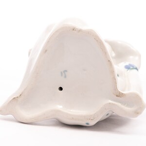 Peut inclure: Figurine en porcelaine blanche, vue de dessous, avec un trou et le chiffre "15" marqu&eacute; sur la base. La figurine pr&eacute;sente des motifs floraux bleus et un design drap&eacute;. L'ensemble est pos&eacute; sur un fond blanc.