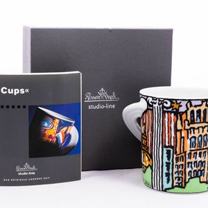 May include: A white ceramic mug featuring a colourful illustration of a city skyline. The mug has two handles and is part of a set called "City Cups". The mug is packaged in a grey box with the brand name "Rosenthal studio-line" printed on it.