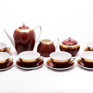Puede incluir: Un juego de té vintage con un diseño marrón y dorado. El juego incluye una tetera, una jarra de crema, un azucarero y seis tazas y platillos.
