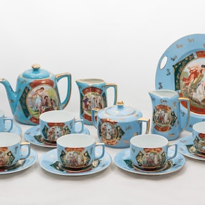 Puede incluir: Un juego de té antiguo completo en azul claro con detalles dorados. El juego incluye una tetera, azucarero, jarra de crema, tazas, platillos y una bandeja. Cada pieza presenta una escena pintada detallada.