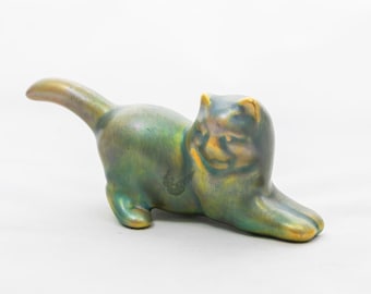 Peut inclure: Figurine de chat en céramique, en position couchée, avec un glaçage irisé vert et or. Le chat a les pattes avant tendues et la queue courbée vers le haut. La figurine mesure environ 15 cm de long.