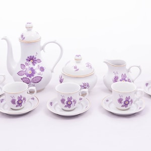 Puede incluir: Un juego de té floral morado con tetera, jarra de crema, azucarero y cuatro tazas y platillos.