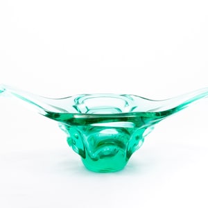 Puede incluir: Un cuenco de vidrio verde azulado con dos asas. El cuenco tiene una forma orgánica única y una superficie texturizada.