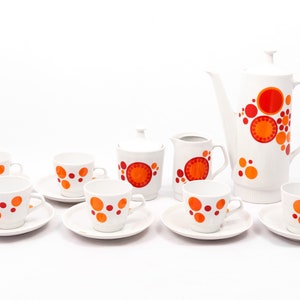 May include: A white ceramic tea set with orange and red circles. The set includes a teapot, creamer, sugar bowl, and six cups and saucers.