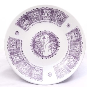 Könnte beinhalten: Ein weißer Keramikteller mit einem violetten Design. Das Design zeigt im Zentrum ein Frauen Gesicht, umgeben von einem Kreis aus kleinen Punkten. Der Rand des Tellers hat ein sich wiederholendes Muster aus kleinen Häusern und anderen Designs.