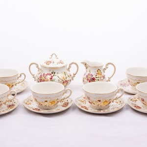 Puede incluir: Un juego de té de porcelana blanca con detalles florales y dorados. El juego incluye una tetera, una jarra de crema, un azucarero y cuatro tazas de té y platillos.