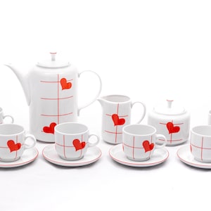May include: A white porcelain tea set with red hearts on a white background. The set includes a teapot, creamer, sugar bowl, and six cups and saucers.