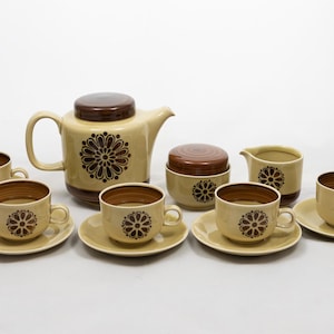 Pode incluir: Conjunto de chá vintage em bege e castanho. O conjunto inclui uma chaleira, açucareiro, cremeira e seis chávenas com pires. Cada peça apresenta um design floral.