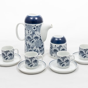 Pode incluir: Um conjunto de chá de cerâmica com um padrão floral em azul marinho e branco. O conjunto inclui uma chaleira alta, um açucareiro e quatro xícaras com pires. As xícaras e os pires têm uma borda azul marinho.