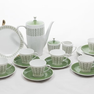 Pode incluir: Um conjunto de chá de cerâmica branca e verde. O conjunto inclui uma chaleira, xícaras, pires, açucareiro, cremeira e prato de servir. As xícaras e a chaleira têm um padrão repetitivo de pequenos pontos verdes.