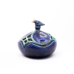May include: A blue ceramic trinket box with a bird finial. The box has a green lattice design and a blue glaze.
