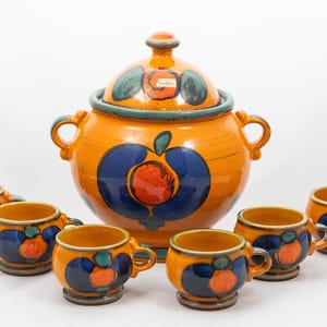 Könnte beinhalten: Ein Keramik-Servier-Set mit einem großen orangefarbenen Topf mit Deckel und sechs passenden Tassen. Das Set ist mit blauen und orangefarbenen Fruchtdesigns verziert. Der Topf hat zwei Griffe. Die Tassen sind 7.6 cm hoch.