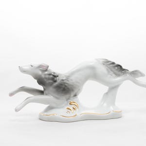 Puede incluir: Una figurita de porcelana de un perro gris y blanco corriendo, con una base con detalles dorados.