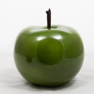 May include: A glossy, green apple with a dark brown stem. The artificial fruit has a smooth, reflective surface and is set against a white background. This decorative apple could be used as a kitchen or dining room accent.